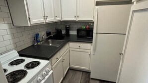 A compact kitchen with white cabinets, a stove, a microwave, and a refrigerator. - The Loft small studio apartment on the 2nd floor.  Private, Small & Affordable (Albert Lea)