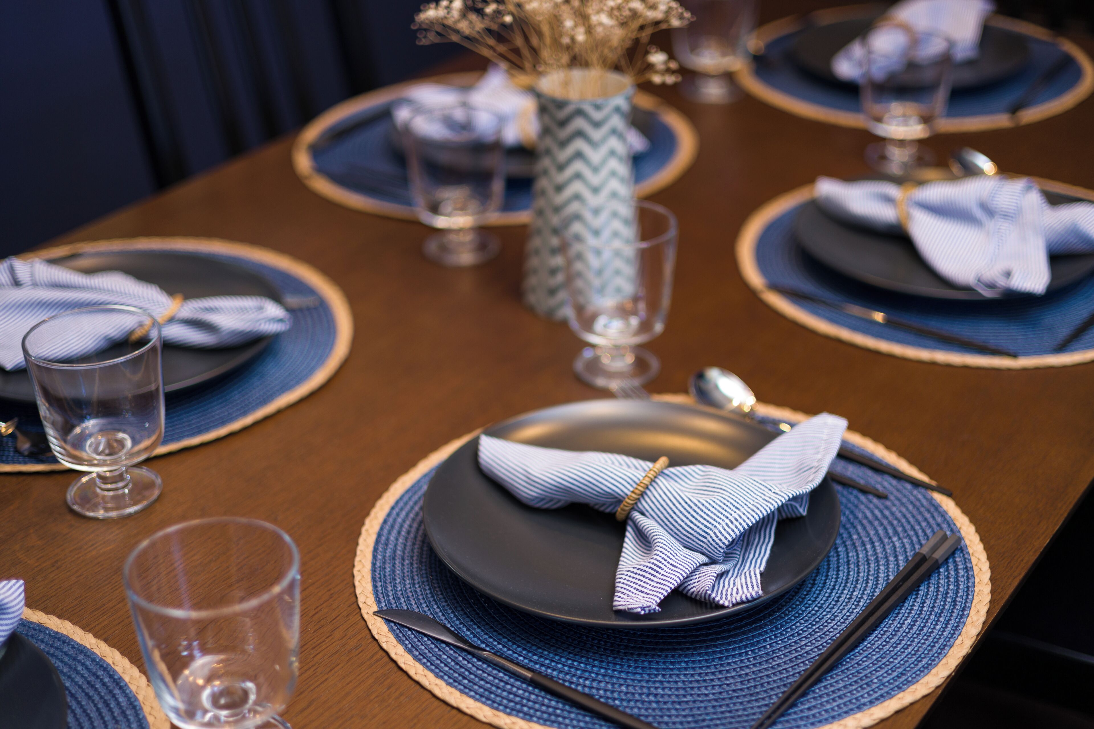 A dining table set with blue placemats, black plates, and clear glasses.