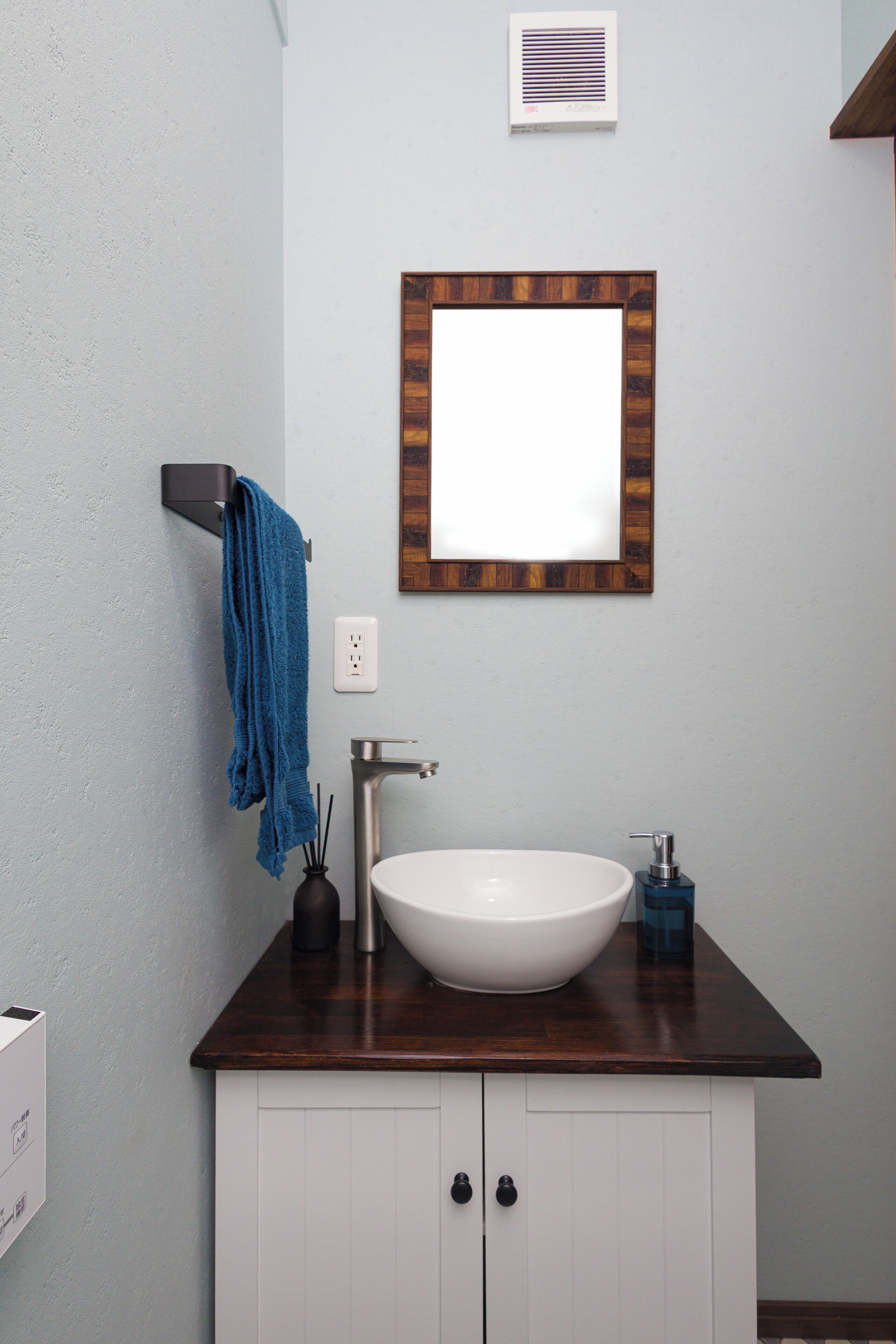 A bathroom with a white sink, a wooden countertop, a blue towel, and a mirror with a wooden frame.