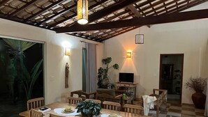 A dining area with a wooden table and chairs, a television, and potted plants.