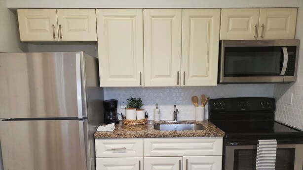 A kitchen with white cabinets, a stainless steel refrigerator, a microwave, and a stove. - Dania Beach 1BR Retreat - Private Entry & Self Check-In (Dania Beach)