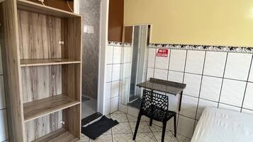 A compact room with a bed, a wooden shelf unit, a small table, and a tiled floor.