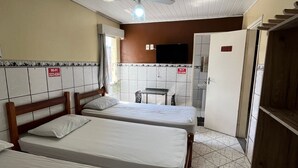 Habitación de hotel con tres camas, ventilador de techo, televisión y kitchenette.