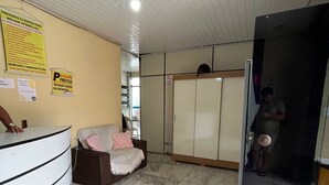 Un área de recepción con un mostrador blanco curvo, una zona de estar con un sofá marrón y una manta rosa, un ventilador de techo y piso de baldosas.