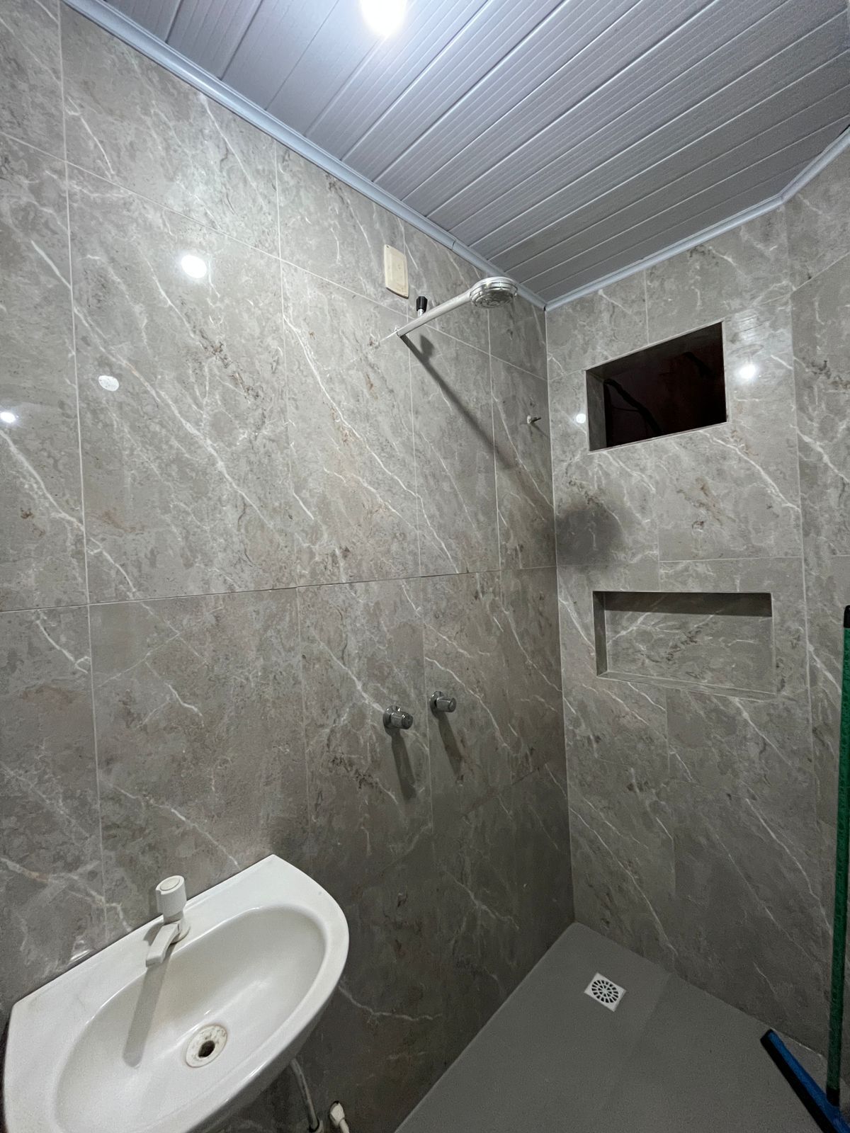 A bathroom with a marble wall, a shower, a sink, and a small window.