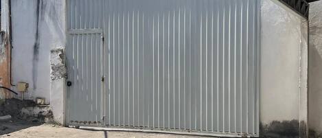 Un área cercada con techo de lámina metálica corrugada, piso de concreto y portón de metal blanco.