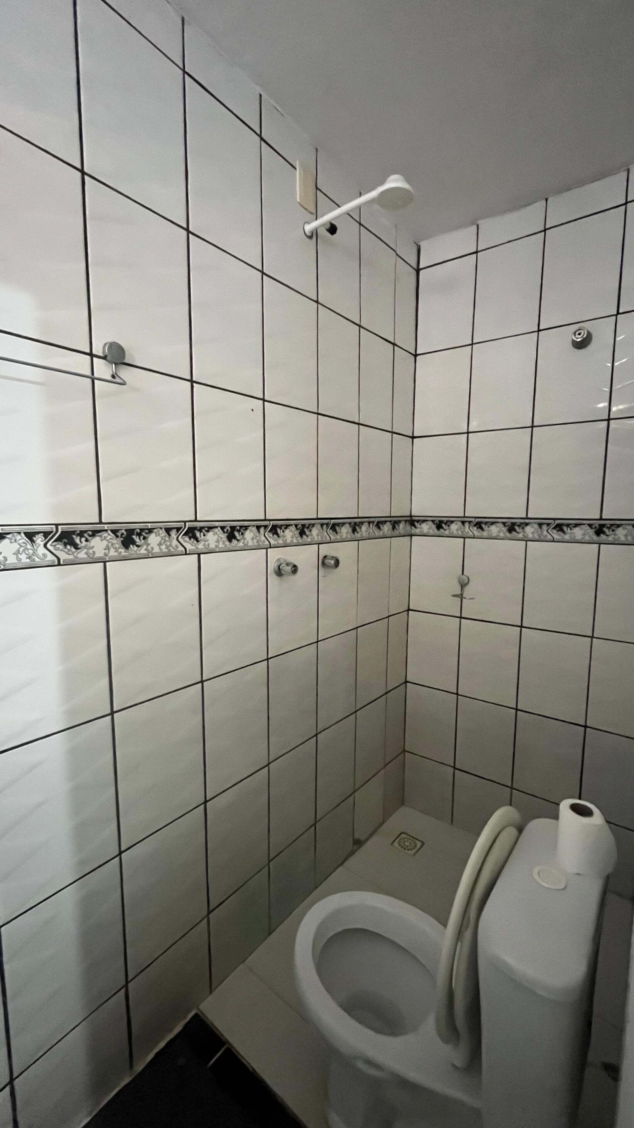 Un baño pequeño con azulejos, un inodoro, un secador de manos y un dispensador de toallas de papel.