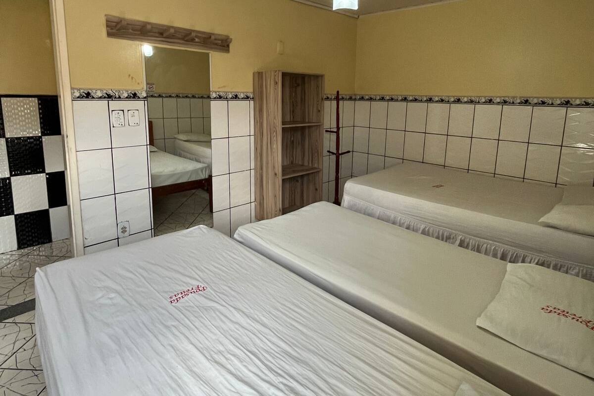 Hotellihuone, jossa on kolme erillistä sänkyä, kattotuuletin, peili ja laatoitettu seinä.