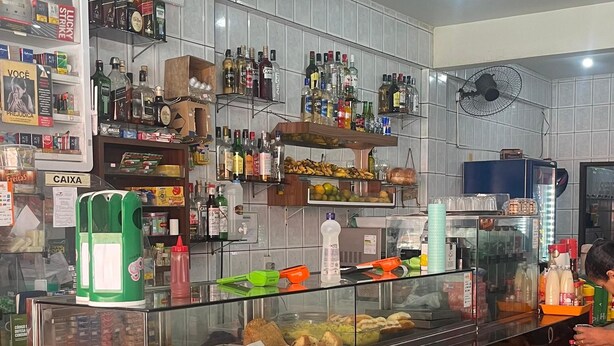 Interior de un restaurante con mostrador exhibiendo alimentos, estantes con botellas y un ventilador en el techo.