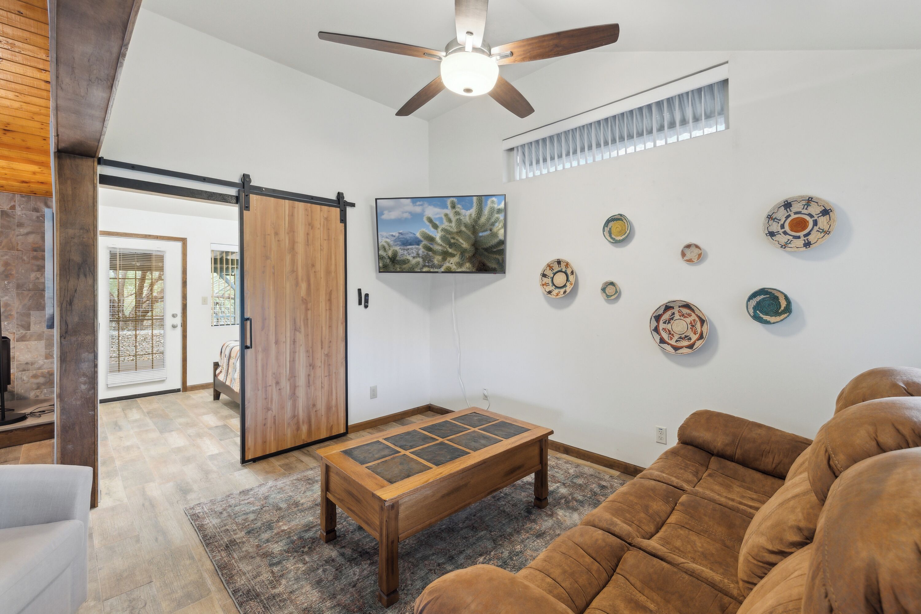A living room with a brown sofa, a wooden coffee table, a ceiling fan, and decorative plates on the wall.