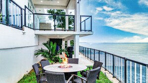 Une terrasse avec une table ronde et des chaises, un foyer extérieur et une vue sur l’océan.