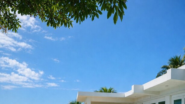 Un couple est assis au bord d’une piscine, avec vue sur l’océan et un bâtiment moderne doté de grandes fenêtres.