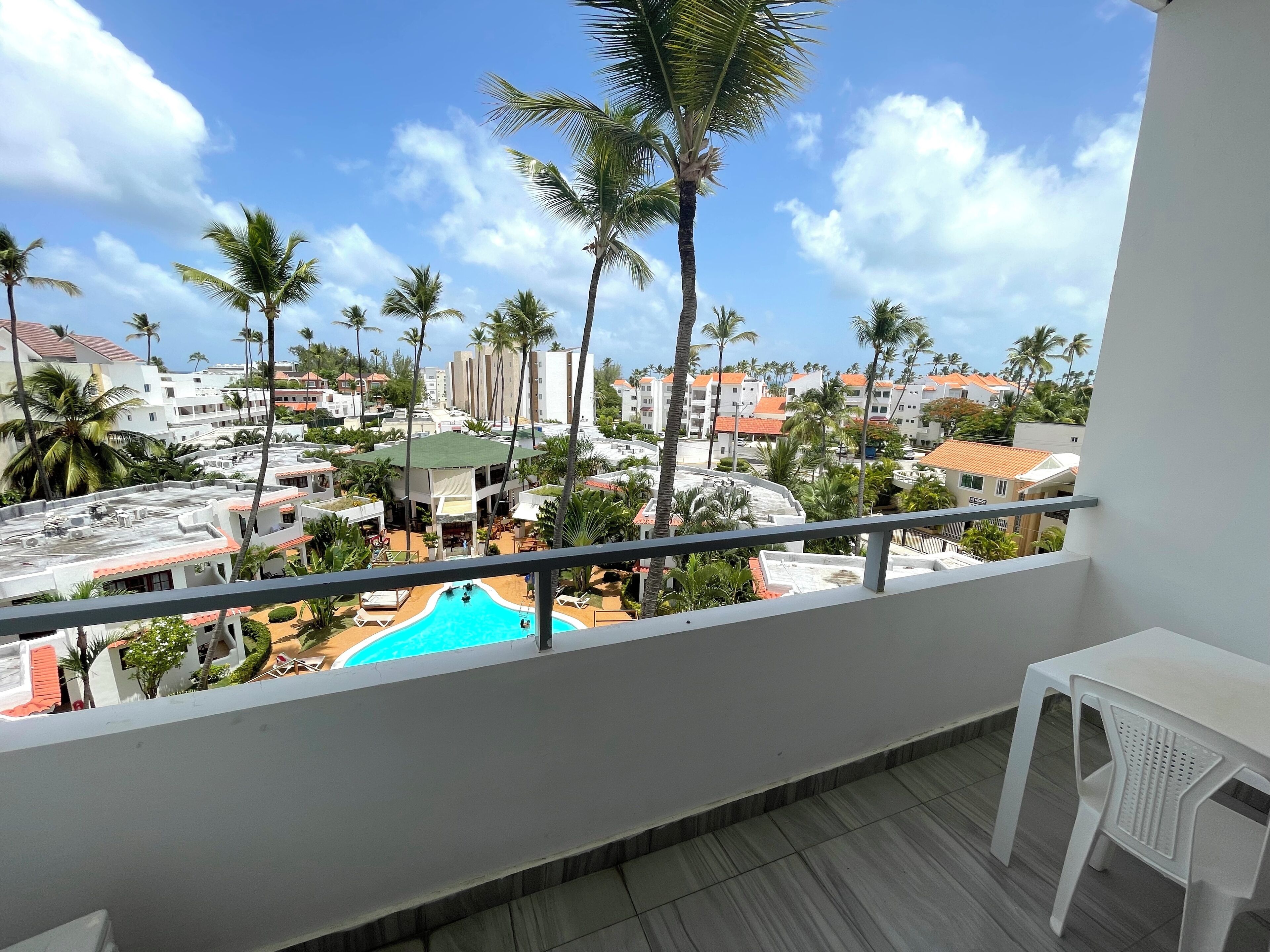 A balcony with a view of a swimming pool, palm trees, and surrounding buildings.