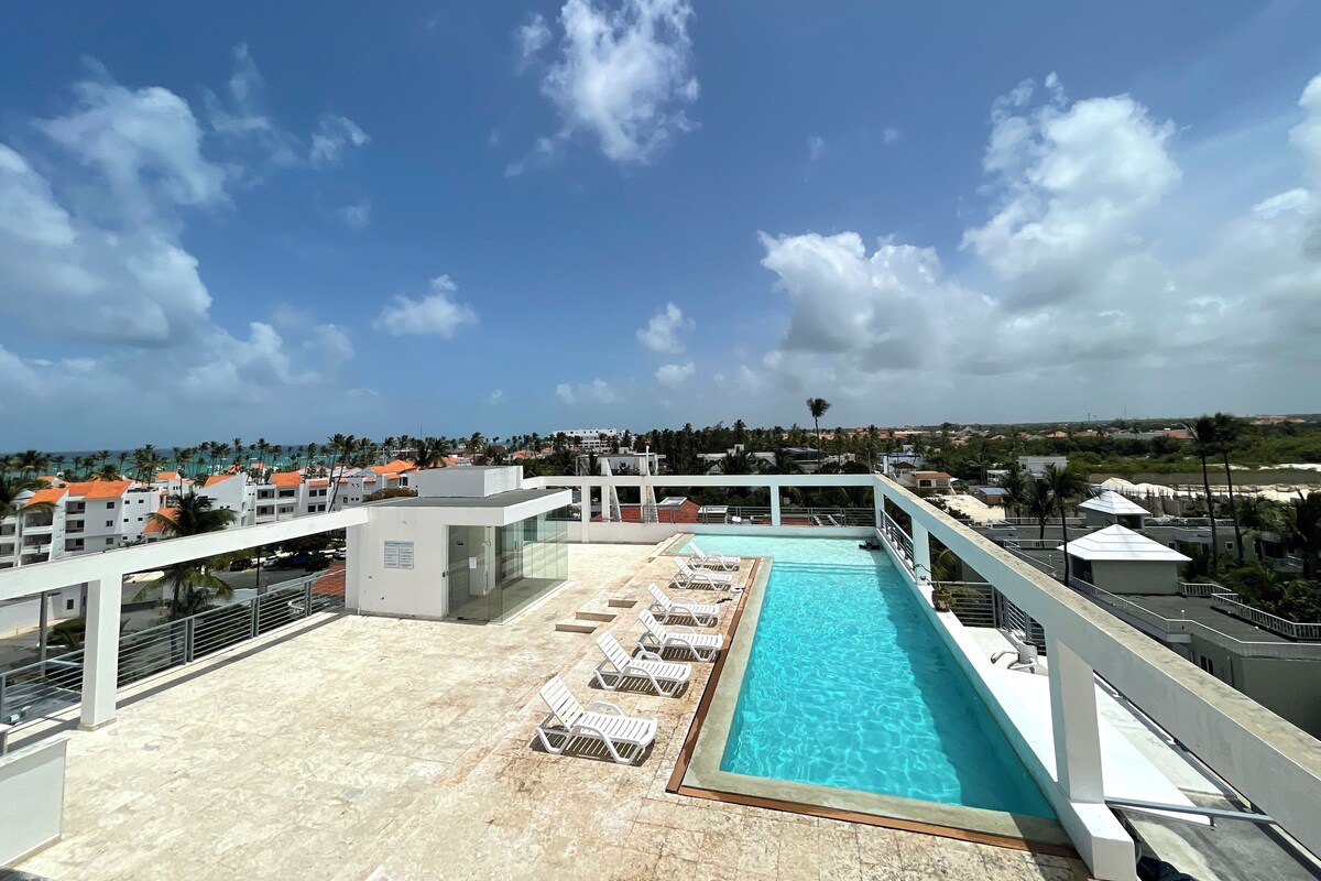 A rooftop pool area with lounge chairs and a clear view of the surrounding buildings and landscape.