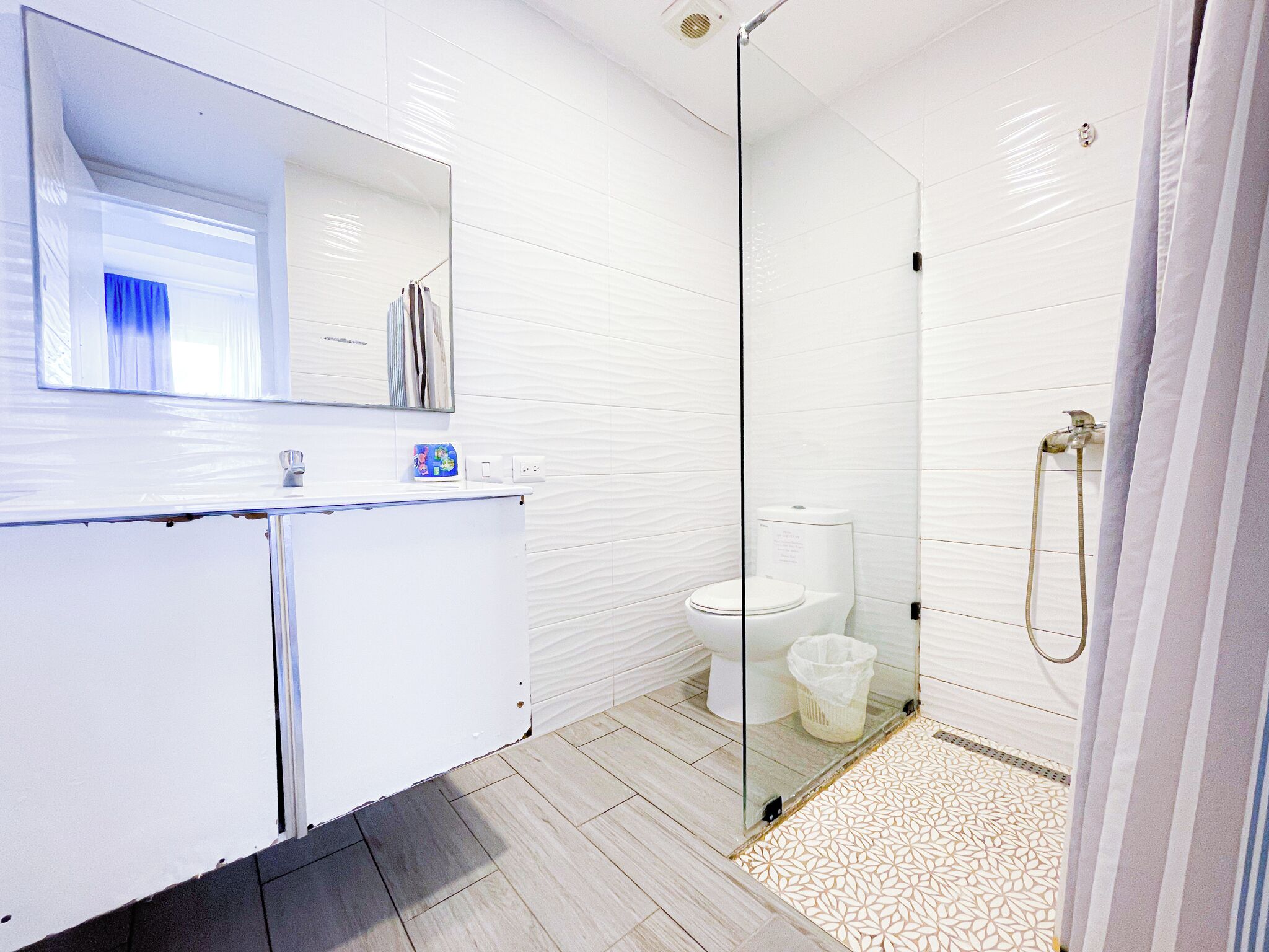A modern bathroom with a glass shower enclosure, white tiled walls, and a patterned floor.