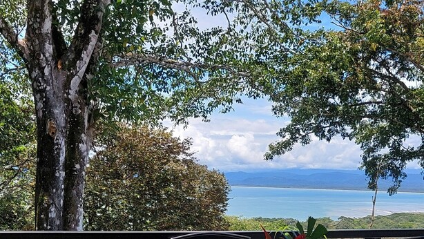 A terrace with a table and chairs overlooking a scenic view of a body of water and distant mountains. - 2 bedroom home with ocean and jungle views in Pavones. Views of the point break. (Pavones)