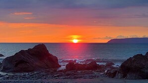 A sunset over a rocky coastline with the sun setting on the horizon. - 2 bedroom home with ocean and jungle views in Pavones. Views of the point break. (Pavones)