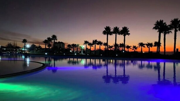 A nighttime view of a swimming pool with palm trees and a sunset in the background. - Spacious Apartment in Algarrobo in Laguna Vista with Ocean / Sea view (Algarrobo)