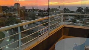 A balcony with a glass railing overlooking a cityscape during sunset. - Spacious Apartment in Algarrobo in Laguna Vista with Ocean / Sea view (Algarrobo)