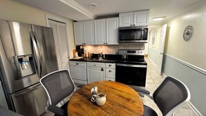 A compact kitchen with stainless steel appliances, white cabinetry, and a round wooden table with chairs.