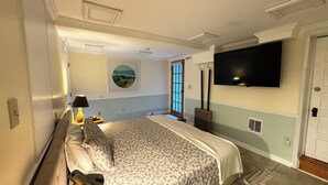 A bedroom with a bed, a TV mounted on the wall, a window with blinds, and a painting on the wall.