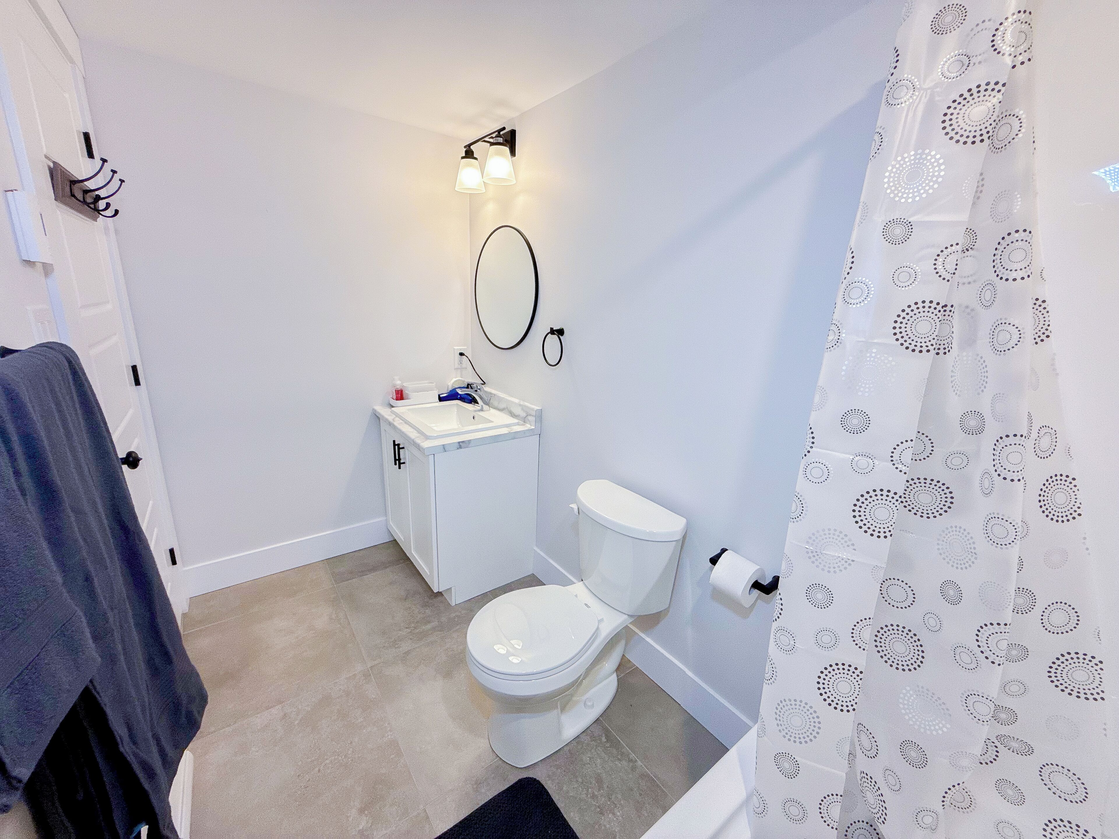 Een kleine, schone badkamer met toilet, wastafel en een douchegordijn met een cirkelpatroon.