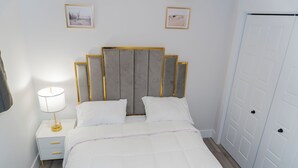 A neatly made bed with a white comforter and pillows, a bedside table with a lamp, and a framed picture on the wall.