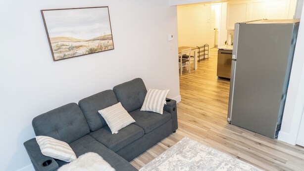 A modern living room with a grey sofa, a patterned rug, and a kitchen area visible through an open door.