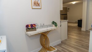 A white console table with a 'Welcome' sign, a small plant, and a framed picture on the wall.