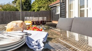Un espace de restauration en plein air avec une table en verre, des assiettes, des couverts, une miche de pain, des fraises et des verres de vin rouge.