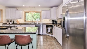 A modern kitchen with white cabinets, stainless steel appliances, and a central island with bar stools. - Quite Lakefront Home on UTV/ATV/Snowmobile trails.  Dog Friendly! (Mercer)