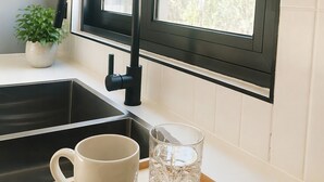 Een keuken met een zwarte kraan, een witte mok en een glas op een houten dienblad.