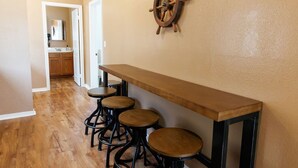A hallway with a wooden bench and stools, a ship's wheel decoration on the wall, and a kitchen area in the background. - Walk to DTLB, RetroRow, & Beach! (Long Beach)