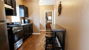 A compact kitchen with dark cabinetry, a stove, and a microwave. There is a wooden bar counter with stools. - Walk to DTLB, RetroRow, & Beach! (Long Beach)