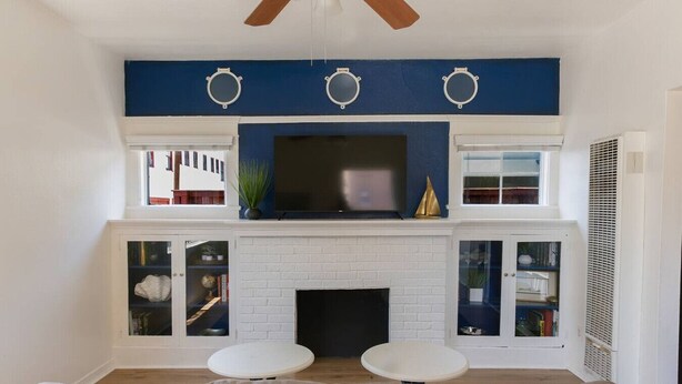 A living room with a white brick fireplace, two white round tables, a beige sofa, and a large flat-screen TV mounted above the fireplace. - Walk to DTLB, RetroRow, & Beach! (Long Beach)