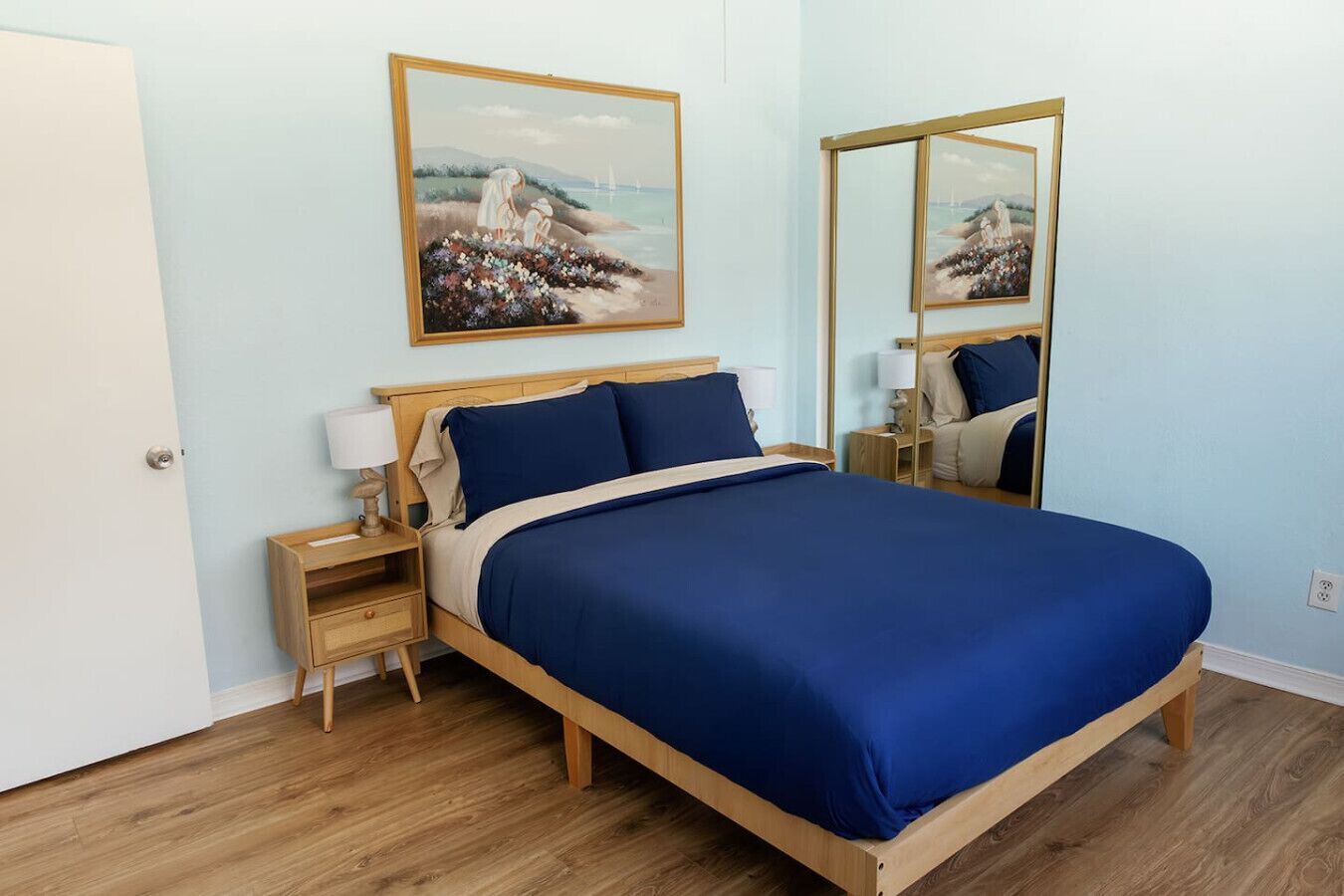 A bedroom with a bed, nightstands, a mirror, and a painting on the wall.