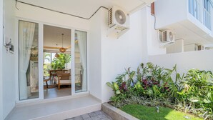 A modern house with a glass door leading to a patio with a dining set and potted plants. - Sunny Villa Tumbak Bayuh (Canggu)