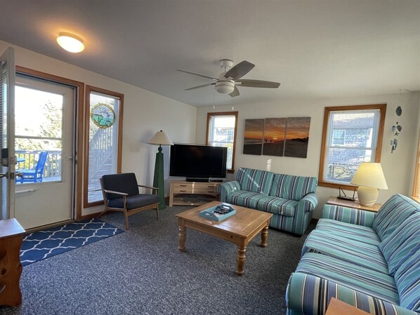 A living room with a sofa, armchair, coffee table, TV, and ceiling fan. - Chasing Sunsets Dog-friendly home w/deck and ocean view (HATTERAS)