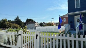 Un barrio residencial con una valla de piquetes blancos, una casa azul y varias banderas.