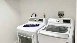 Lavandería con dos lavadoras blancas y una secadora, techo blanco y piso de madera.