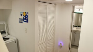 Un cuarto de lavado con lavadora, un armario blanco con puertas persianas y un baño pequeño con lavamanos y espejo.