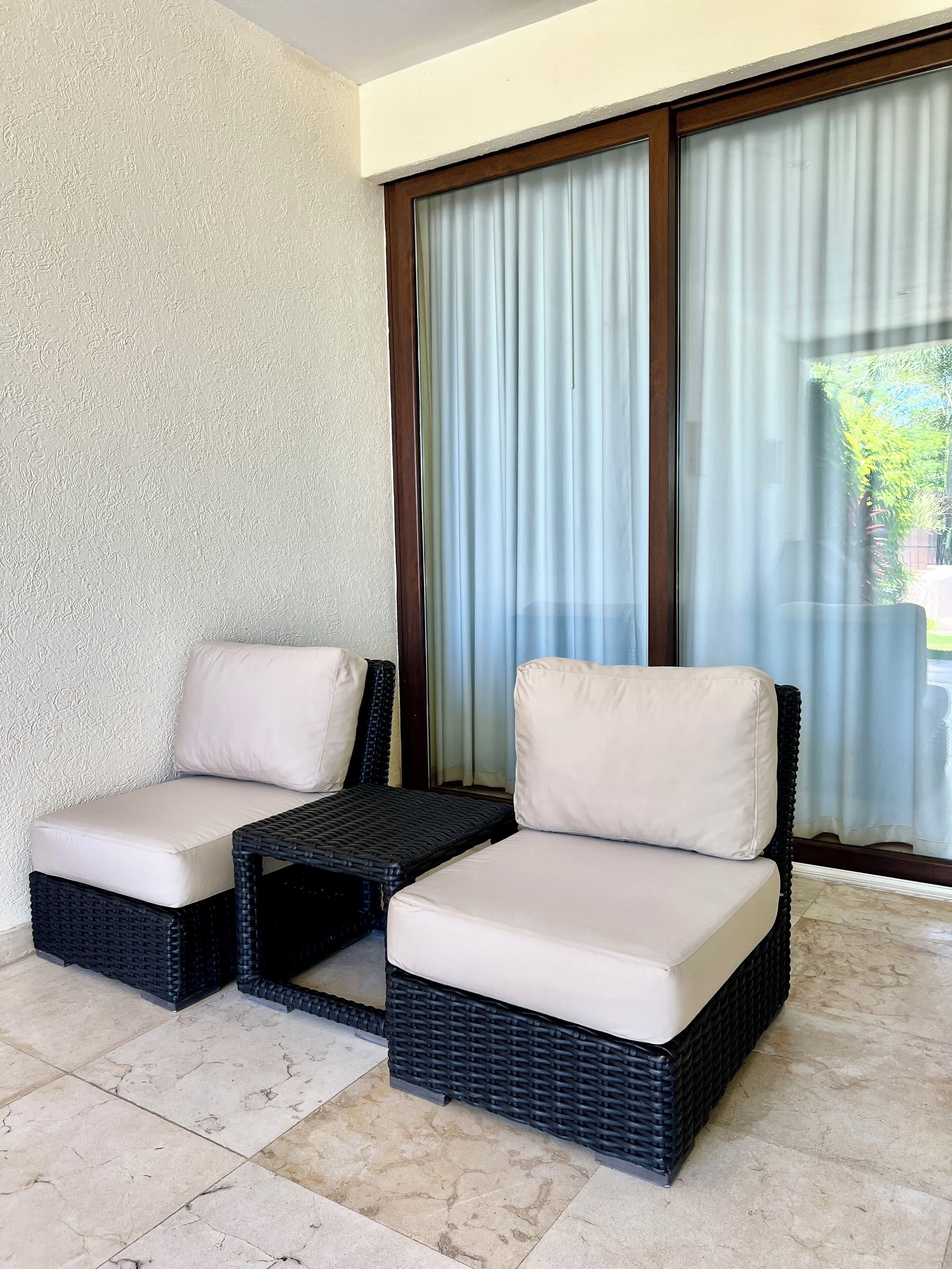 Un rincón con asientos que incluye dos sillones acolchados y una mesita, ubicado cerca de un ventanal con cortinas.