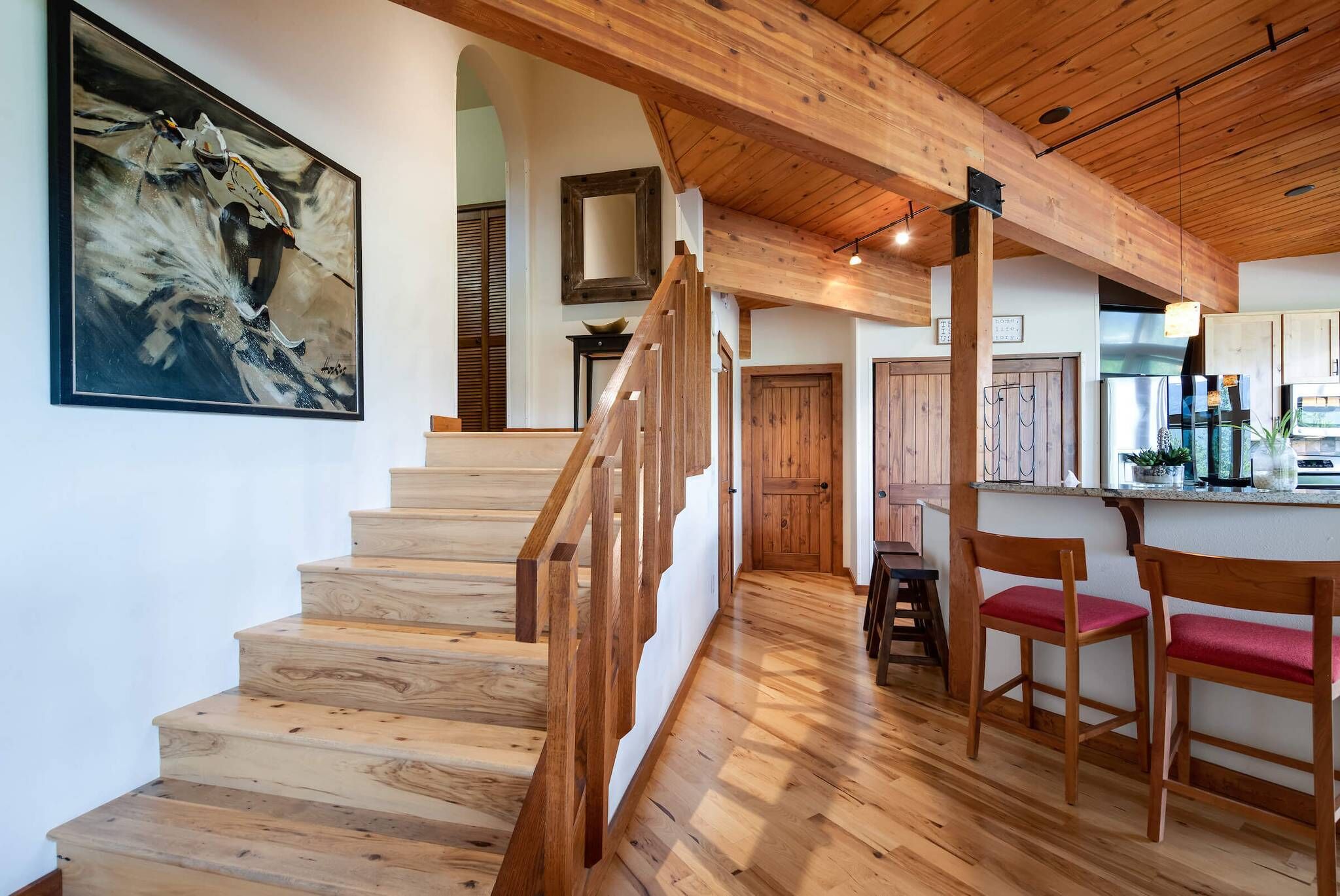 Una escalera de madera que lleva a una zona de cocina con sillas de madera y una mesa de comedor.