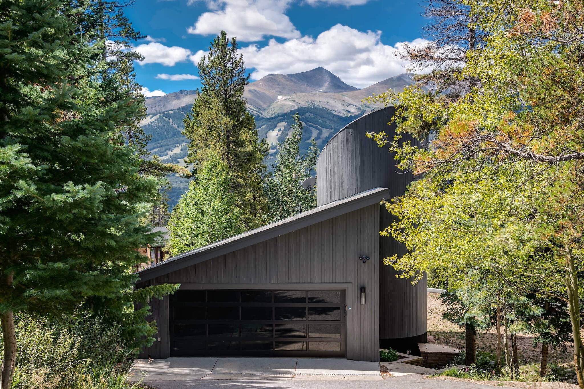 Un bâtiment moderne doté d’un garage, entouré d’arbres et avec des montagnes en arrière-plan.