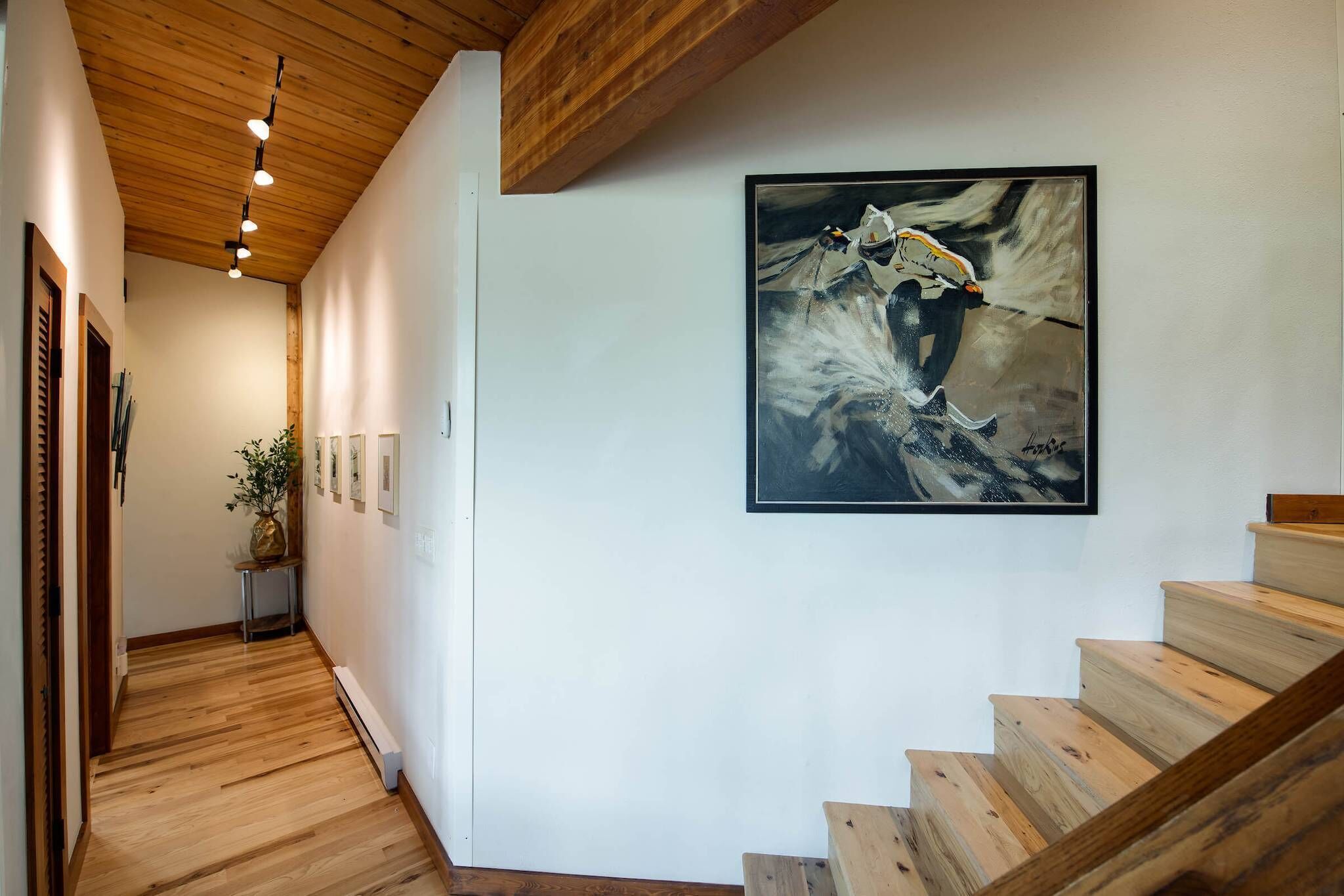 A wooden staircase with a framed painting of a horse on the wall.