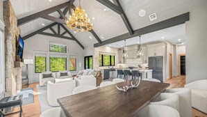 A spacious living area with a large wooden dining table, white sofas, and a stone fireplace. - 330 South Peak - Hot Tub - Timbertown Lift - Pemi River Access - Loon Mtn (Lincoln)