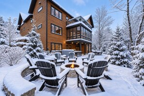 A multi-story lodge with a fire pit and Adirondack chairs in a snowy outdoor area.
