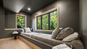 A compact bedroom with a single bed, two windows, a small bedside table, and a view of greenery outside. - 330 South Peak - Hot Tub - Timbertown Lift - Pemi River Access - Loon Mtn (Lincoln)