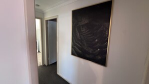 Un couloir avec une œuvre d’art encadrée au mur, un sol recouvert d’une moquette et une porte donnant sur une autre pièce.