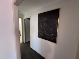 Un pasillo con una obra enmarcada en la pared, suelo alfombrado y una puerta que da a otra habitación.